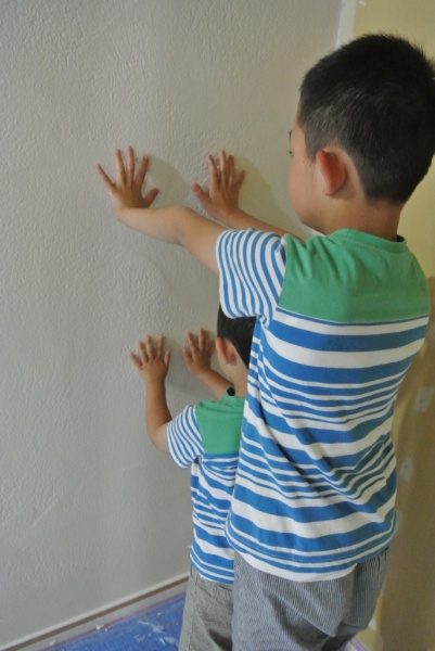 兄弟2人が漆喰の壁に向かって手を押し当てて手形を付けている