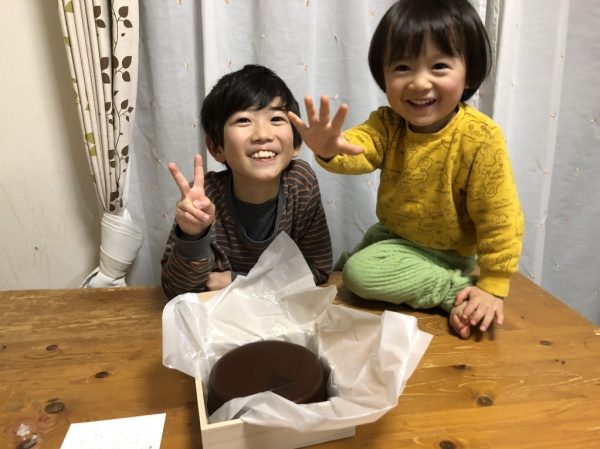 中央に社員さんの子供二人が笑顔で写っている　中央下にチョコレートケーキ