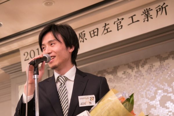 年明け披露会でマイクに向かい笑顔で喋る男性