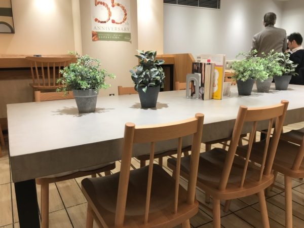パン屋さんのモールテックスグレーのテーブル、机の上には観葉植物や本が置いてある、周りに椅子もある