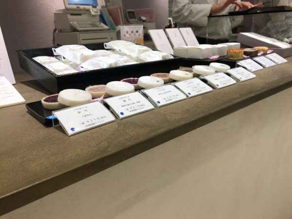 金色のオルトレマテリアで施工されたディスプレイ用カウンターテーブル、巌邑堂日本橋高島屋店、商品の和菓子が並んでおり奥にはレジ、お店の従業員の手元が映っている