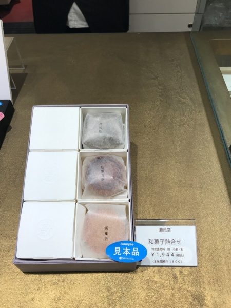 金色のオルトレマテリアで施工されたディスプレイ用カウンターテーブル、巌邑堂日本橋高島屋店、商品の和菓子詰め合わせがある