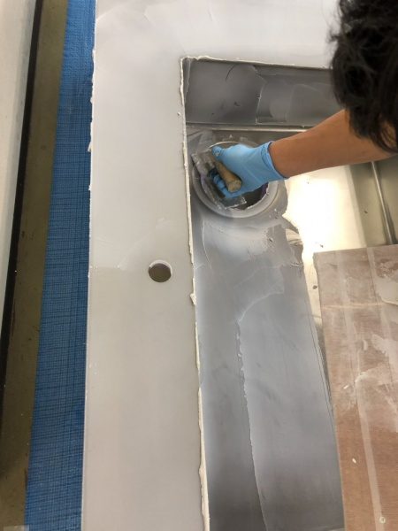 キッチンシンクに下塗りのフォンドフレックスを施工中の職人さん。排水溝周りを塗っている