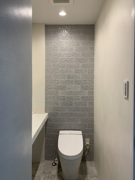 原田左官タイルライブラリーのトイレ(化粧室)。壁は紙をクシャクシャにした模様のタイル、床はセメント調タイルで施工