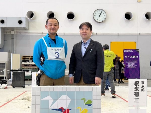 タイル貼り競技の完成した課題を前に記念撮影する根来さんと原田宗亮代表