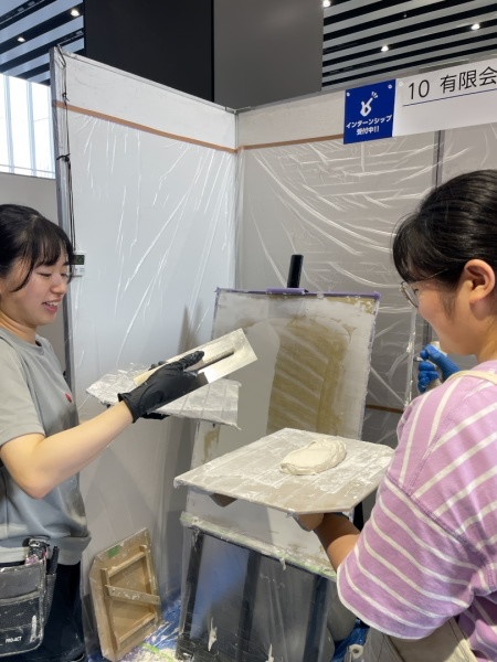就職イベント「高校生フェス」にて塗り壁体験の先生を務める原田左官見習工のNさんと指導を受ける高校生の生徒さん